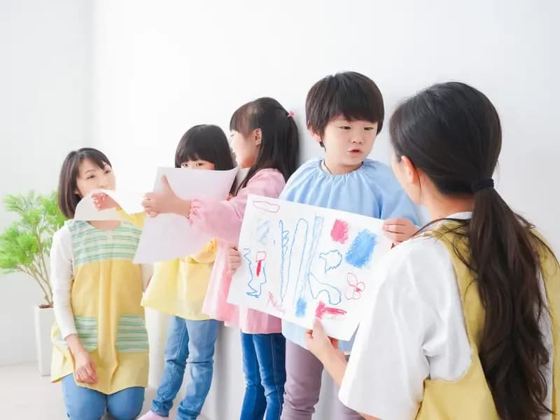 お絵描きした絵を先生に見せる保育園児たちのイメージ