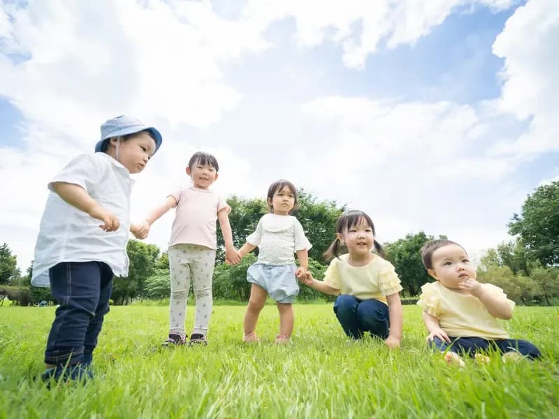 青空の下で手を繋いで一列になる保育園児たちのイメージ