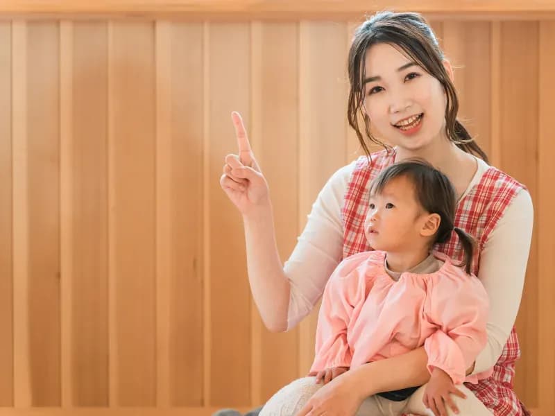 幼児を膝に乗せ笑顔で指をさす女性の画像