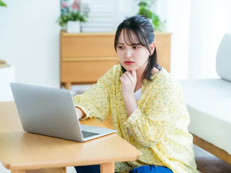 ノートパソコンを見ながら考えている女性のイメージ