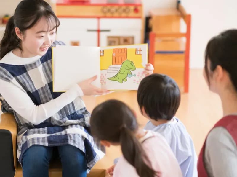 読み聞かせをする保育士と話を聞く園児の画像