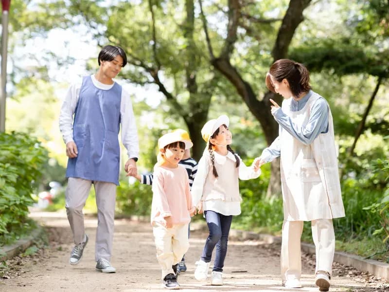 散歩をする男女の保育士と二人の子供の画像