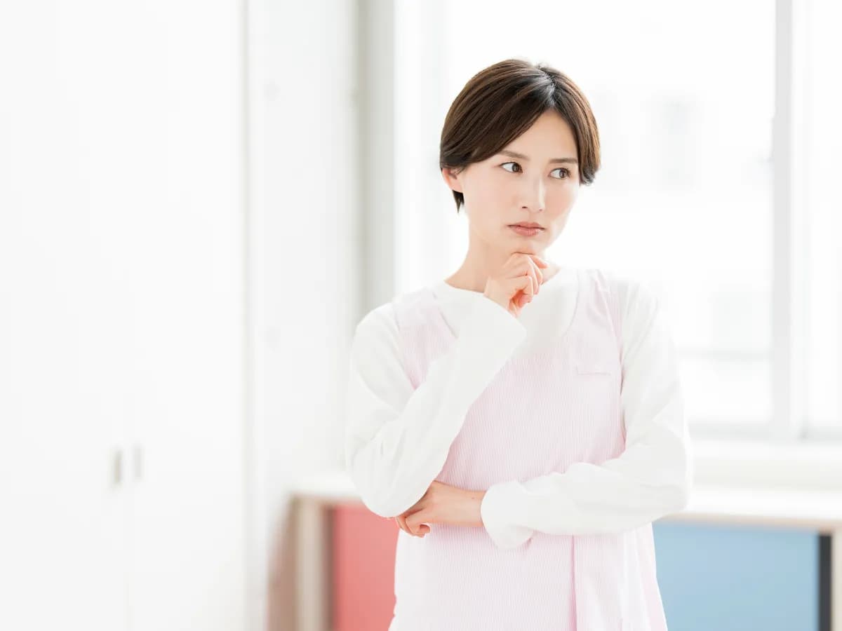 顎に手を当てて考える若い保育士のイメージ
