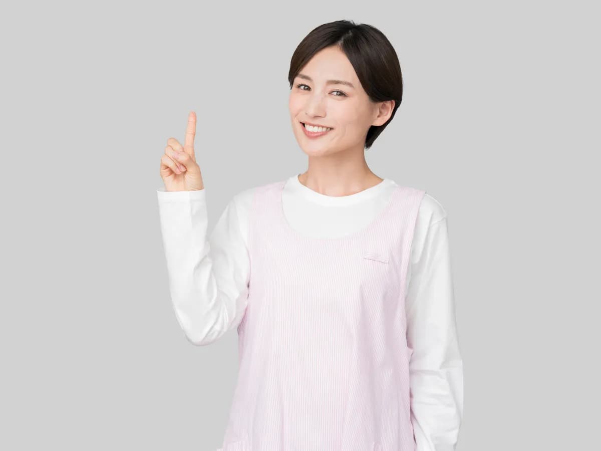 指差しポーズをとる笑顔のエプロン姿の保育士の画像