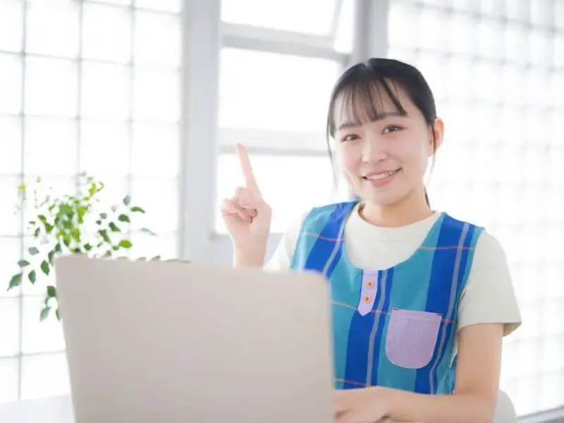 パソコンを前に笑顔の保育士のイメージ
