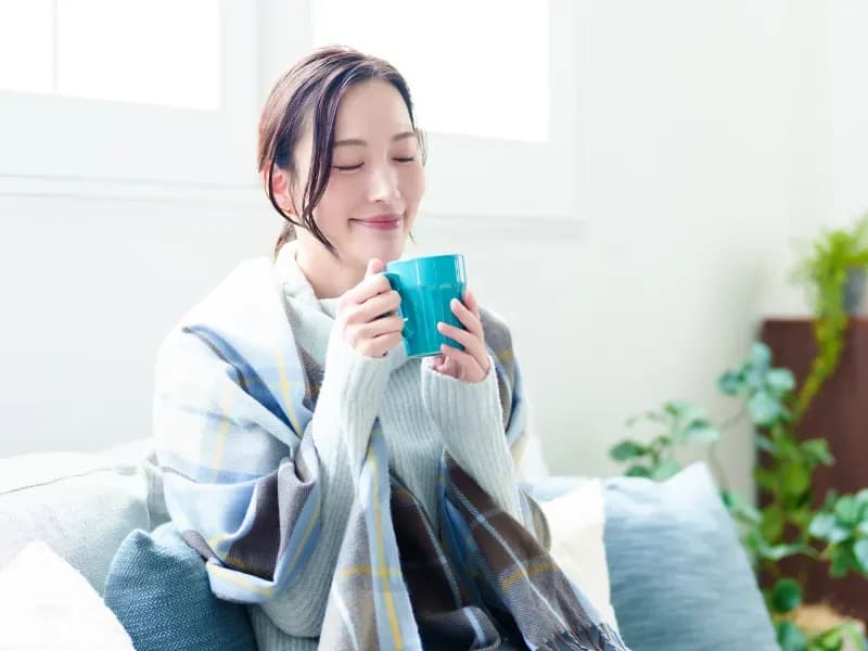 リビングで飲み物を飲む女性の画像