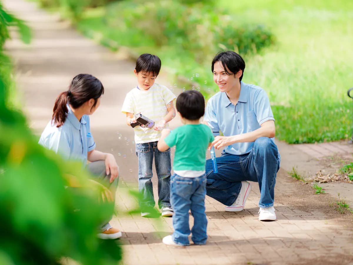 公園でシャボン玉を楽しむ園児と男性と女性の保育士の画像
