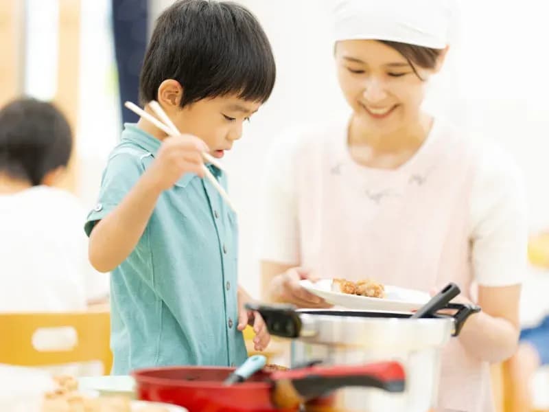 給食を取り分ける保育士と園児の画像